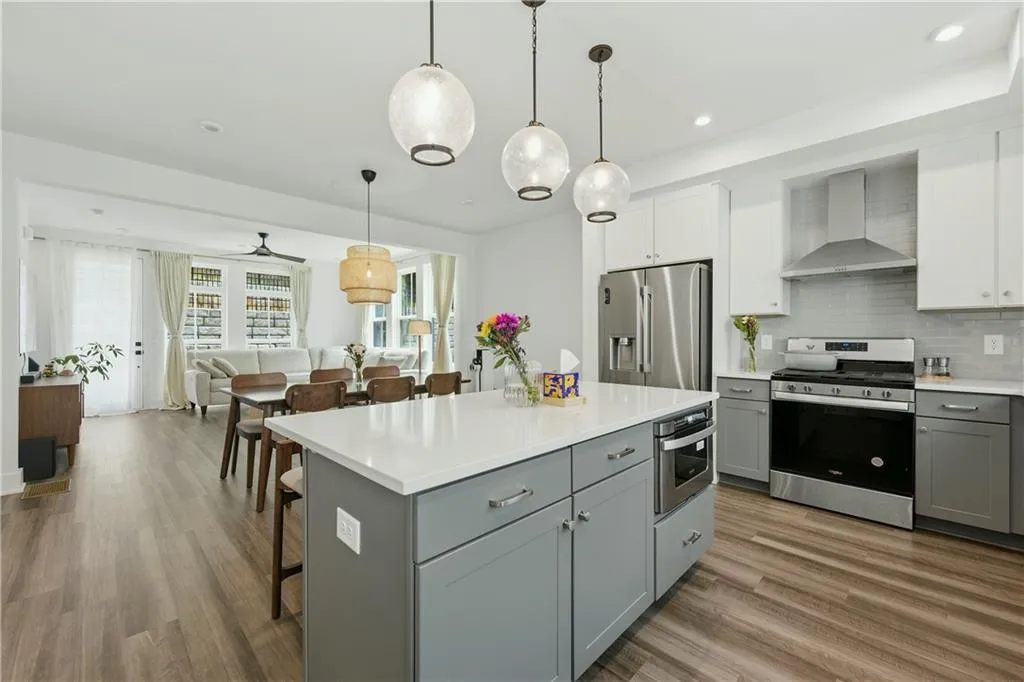 Kitchen island with light-toned countertop, stainless steel appliances, wood-finish flooring, recessed lighting, and pendant lighting fixtures