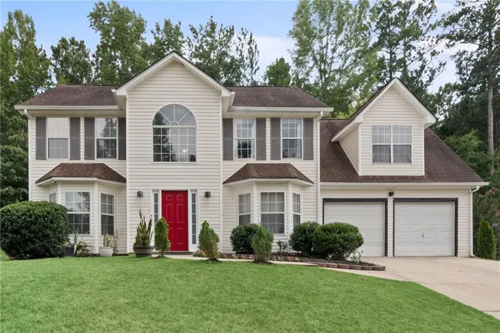 Colonial-style two-story residence featuring a cream-colored vinyl exterior with dark architectural shingles, a prominent arched window detail, and a welcoming red front door
