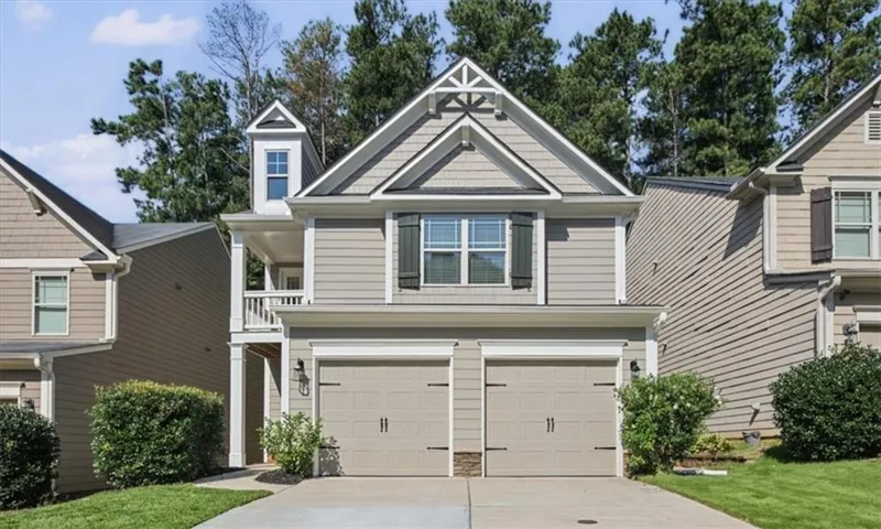 Exterior featuring light gray siding, a two-car garage, a dormer window, decorative gable trim, and dark shutters