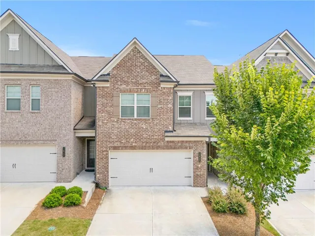 Brick Colonial townhome featuring a two-car garage, gabled roofline with architectural detailing, and mature landscaping