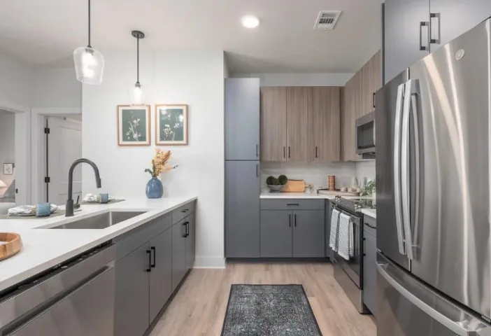 Kitchen with stainless steel appliances, gray cabinetry, hanging light fixtures, light wood-style floors, and light stone counters
