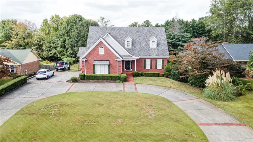 Cape cod home with a front lawn, brick siding, concrete driveway, and view of wooded area