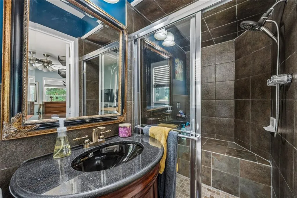 Vanity with dark countertop and undermount sink, framed mirror, and a shower with dark tile surround and glass enclosure