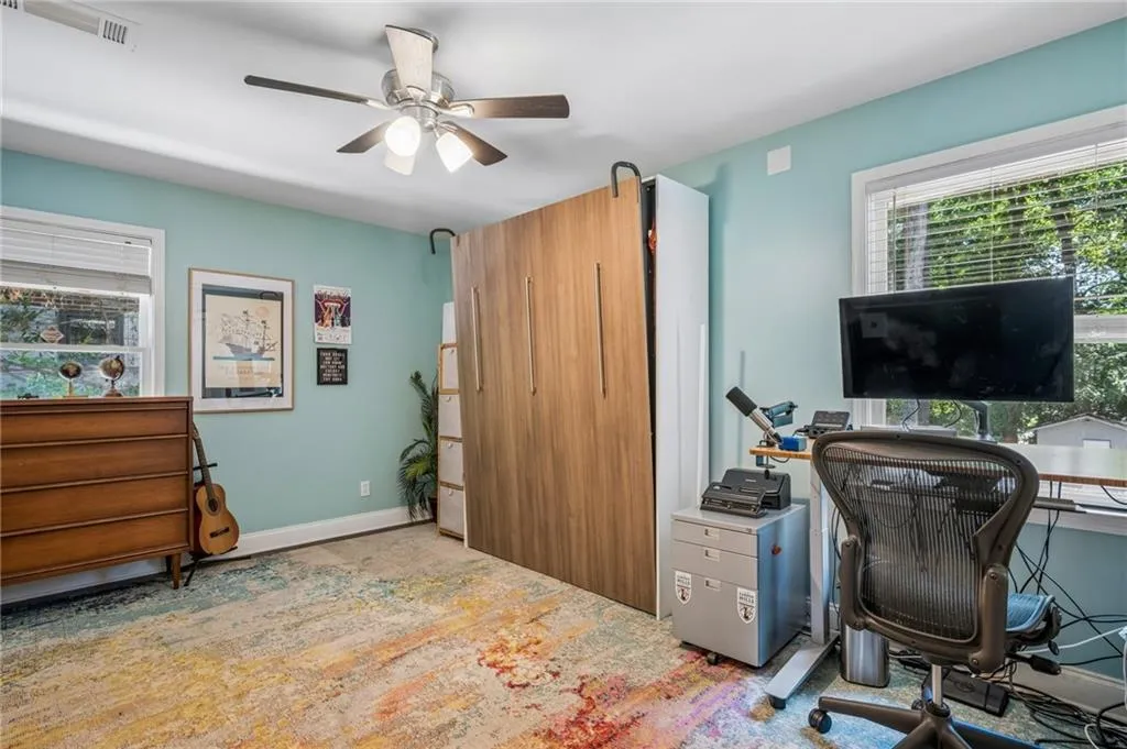 Bright bedroom with turquoise walls, ceiling fan with integrated lighting, wood-finish cabinetry, large windows with natural light, and hardwood flooring accented by an area rug