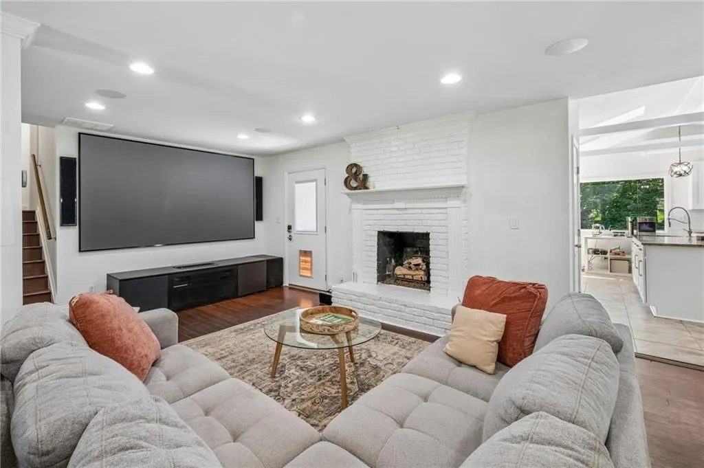 Hardwood flooring, painted brick fireplace, recessed lighting, and a visible kitchen with vaulted ceilings