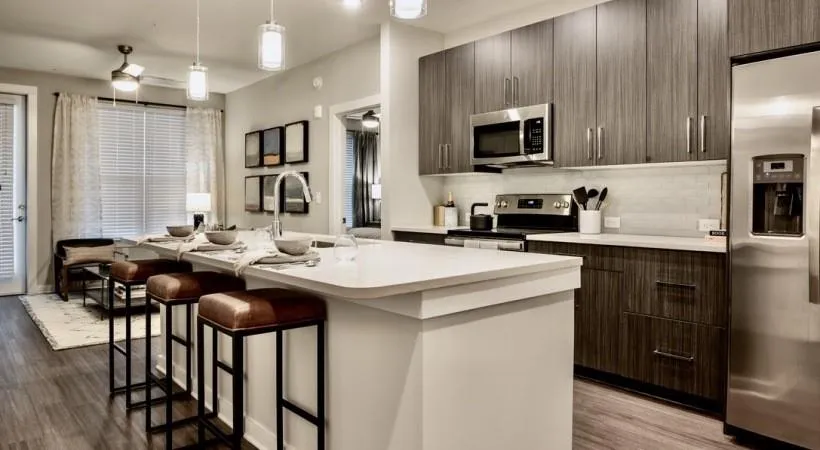 Kitchen with appliances with stainless steel finishes, tasteful backsplash, a center island with sink, light wood-type flooring, and hanging light fixtures