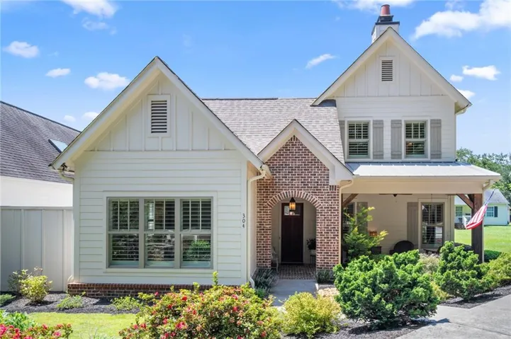 White siding exterior with brick accents, covered front porch, and dormer windows