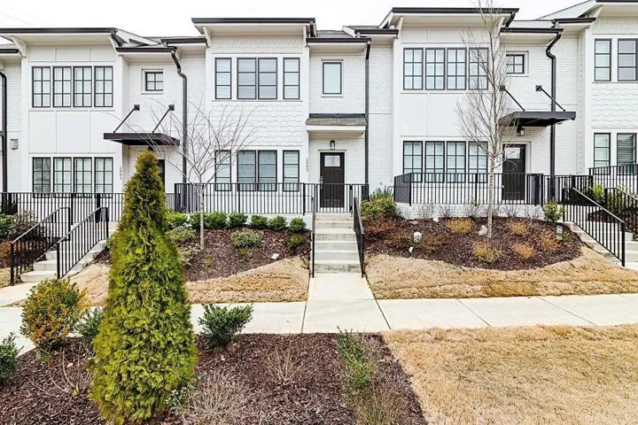 Contemporary exterior with white brick, black-framed windows, dark entry doors, and metal railings