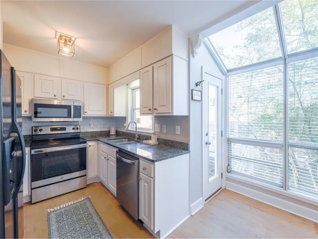 Kitchen featuring stainless steel appliances, dark stone counters, light wood finished floors, and white cabinets