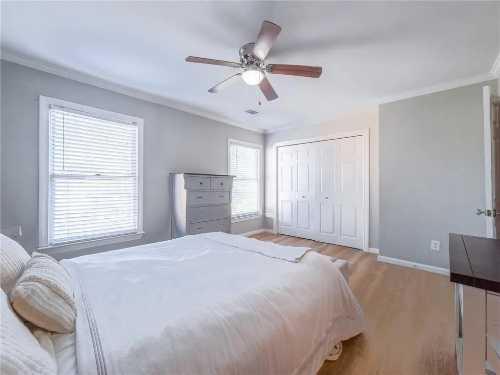 Bedroom with ornamental molding, light wood finished floors, a ceiling fan, and a closet