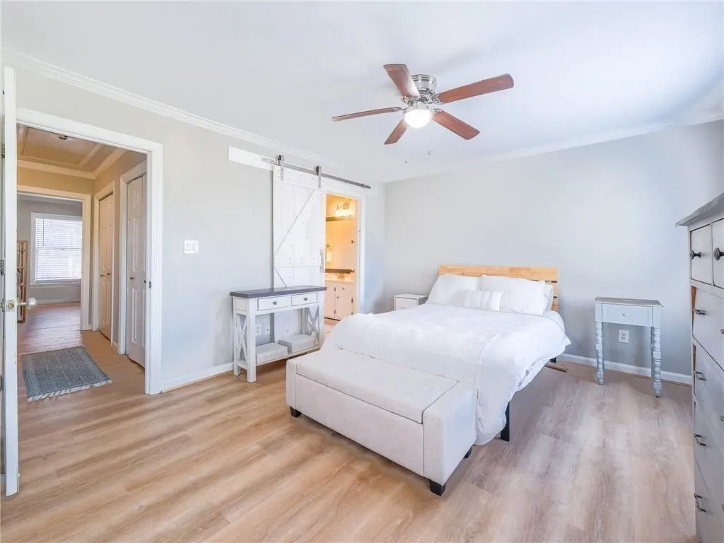 Bedroom featuring ornamental molding, light wood-style flooring, ceiling fan, a barn door, and ensuite bathroom