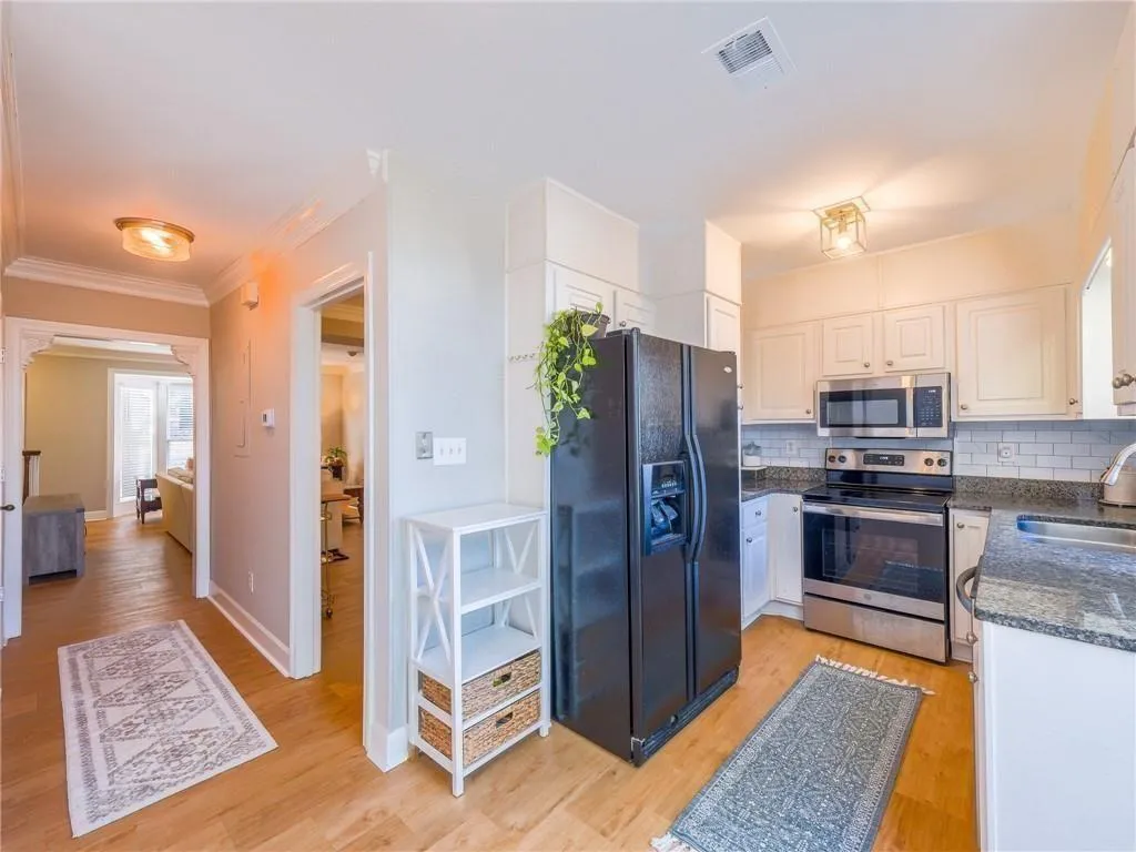 Kitchen featuring appliances with stainless steel finishes, dark stone counters, white cabinets, light wood-style floors, and backsplash