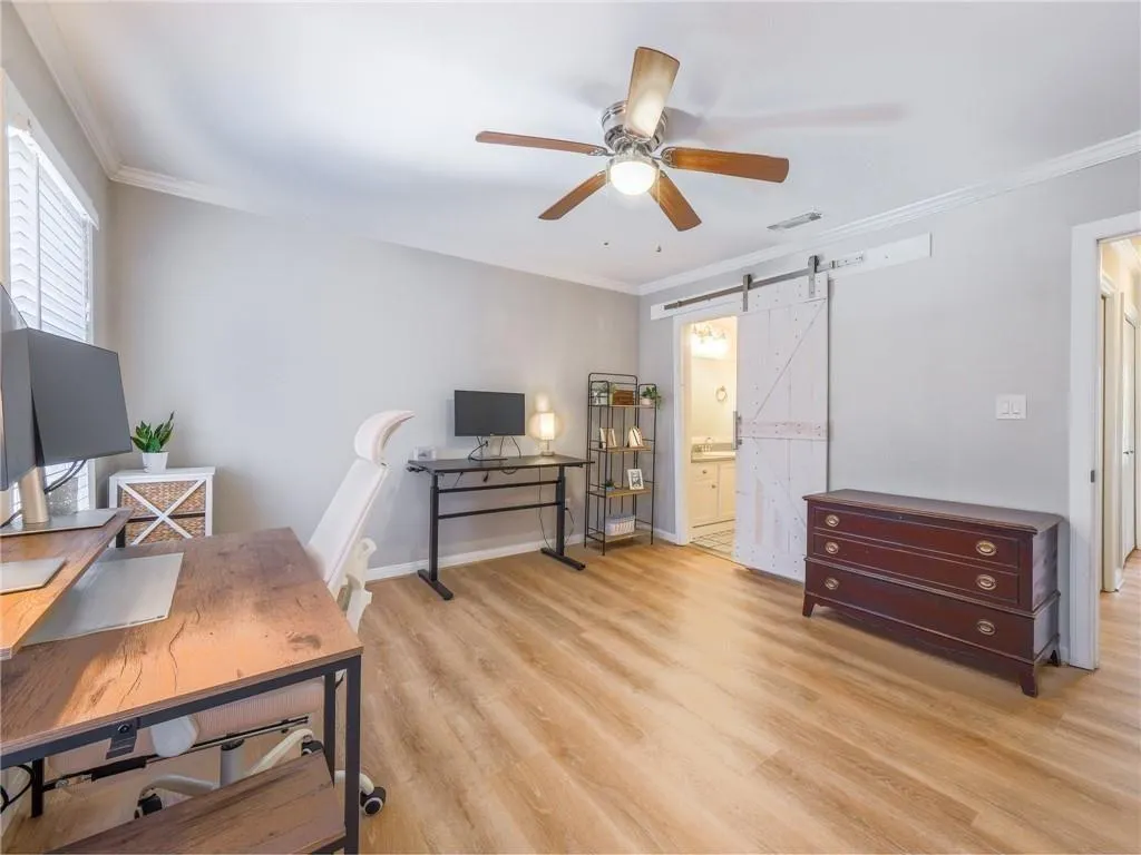 Home office with crown molding, a barn door, a ceiling fan, and light wood finished floors