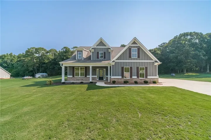 Craftsman-style home featuring gray siding, stone accents, a covered front porch with white columns, dark shutters, and a concrete driveway