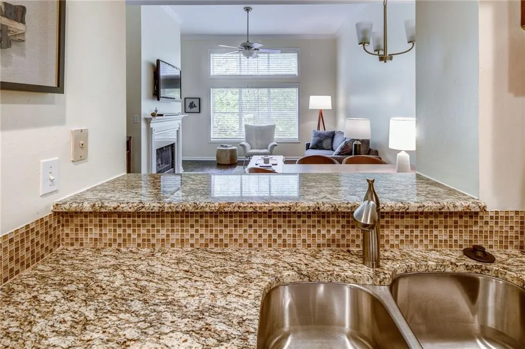 Kitchen featuring crown molding, ceiling fan, a fireplace, light stone counters, and decorative light fixtures