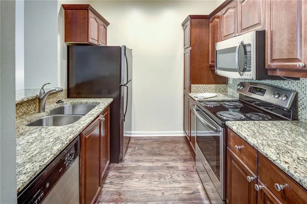 Kitchen featuring stainless steel appliances, decorative backsplash, light stone countertops, and dark wood-type flooring
