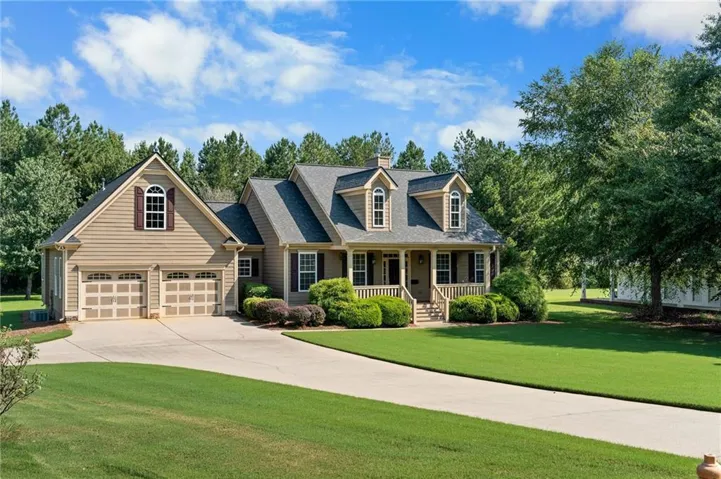 Traditional style exterior with dormer windows, covered front porch, attached two-car garage, and mature landscaping