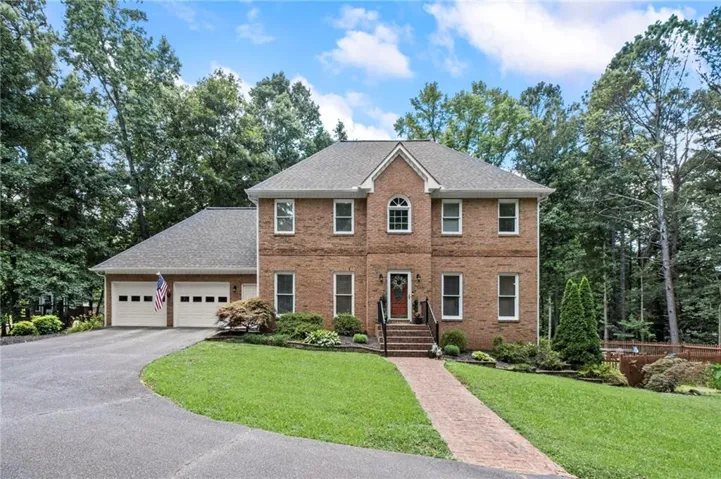 Brick facade residence featuring a two-car garage, paved driveway, and established landscaping