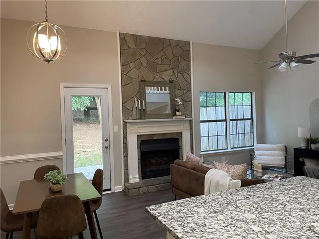 Living room featuring ceiling fan with notable chandelier, a fireplace, a wealth of natural light, and dark wood-type flooring