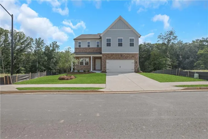 Two-story residence featuring light blue siding, stone veneer accents, an attached garage, a concrete driveway, and a front lawn