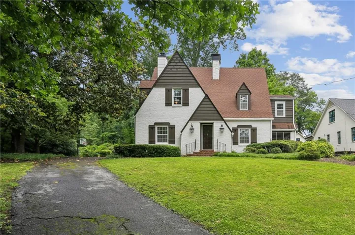 White brick exterior with a brown shingle roof, dormer windows, and a black front door