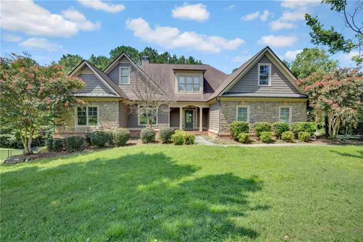 Stone and siding exterior with a gabled roofline, mature landscaping, and a manicured lawn