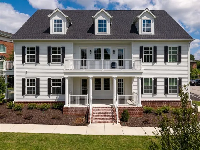 Colonial-style facade featuring white siding, black shutters, dormer windows, and a covered porch with white columns and railings