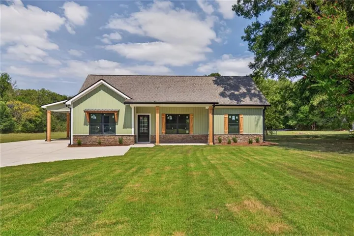 Sage green siding, stone veneer accents, covered front porch, carport, and a concrete driveway