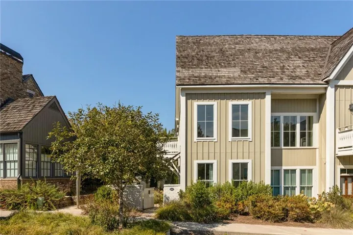 Vertical board-and-batten siding with white trim, multi-pane windows, wood-shingle roof, and mature landscaping