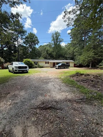 Ranch-style exterior with a covered entry and dual front windows, set back from a gravel driveway