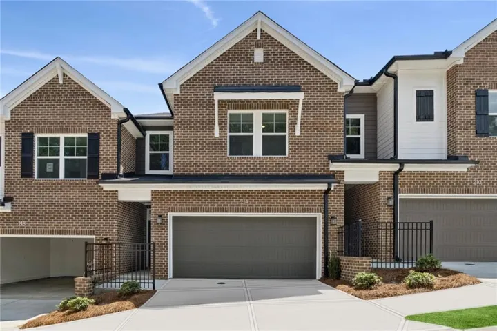 Contemporary brick townhome featuring a two-car garage with dark gray paneling, large multi-pane windows with dark frames, and clean geometric rooflines with mixed material accents including brick and cream-colored siding