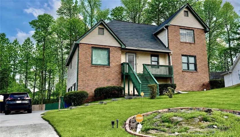 Multi-level residence featuring a brick and siding exterior, a dark shingle roof, and an elevated wooden porch with stairs