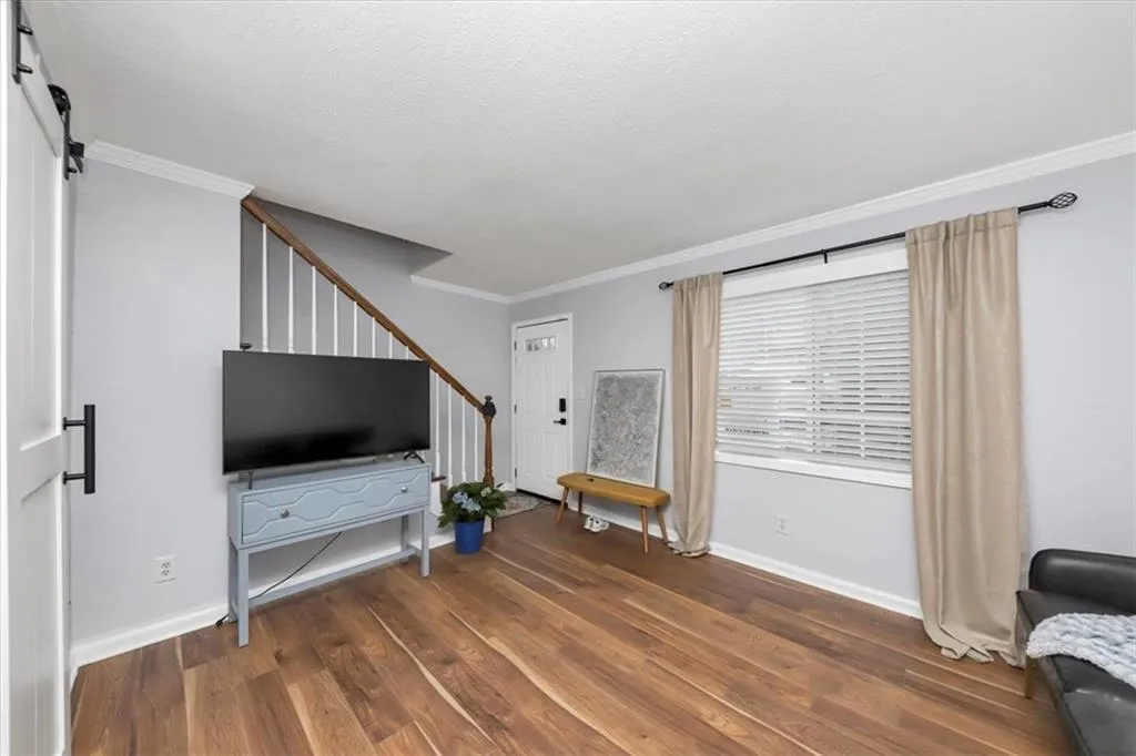 Living room with a barn door, ornamental molding, dark wood-type flooring, and a textured ceiling