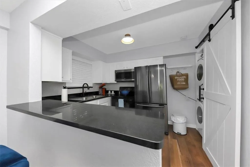 Kitchen featuring kitchen peninsula, stacked washer and clothes dryer, a barn door, white cabinets, and appliances with stainless steel finishes