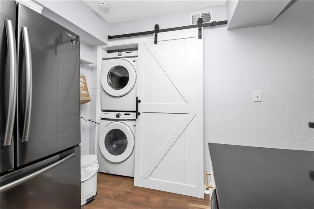 Laundry area with a barn door, stacked washing maching and dryer, and dark hardwood / wood-style flooring