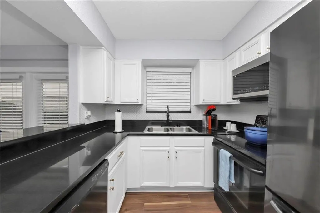 Kitchen with dark hardwood / wood-style flooring, sink, black appliances, and white cabinetry