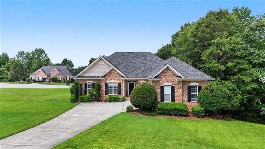 Brick exterior with a gabled roofline, concrete driveway, established landscaping, and mature trees