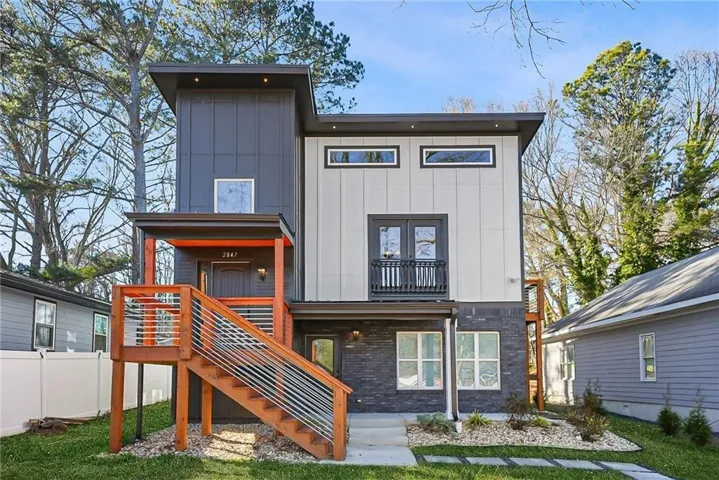 Contemporary exterior with varied siding textures, a covered entry, wood-finish stairs with cable railings, a second-story balcony with a railing, and square paver landscaping
