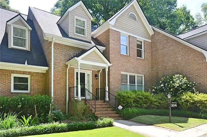 Brick exterior residence with dormer windows, featuring a covered front entry with steps and a black wrought iron railing, surrounded by mature landscaping and a manicured lawn