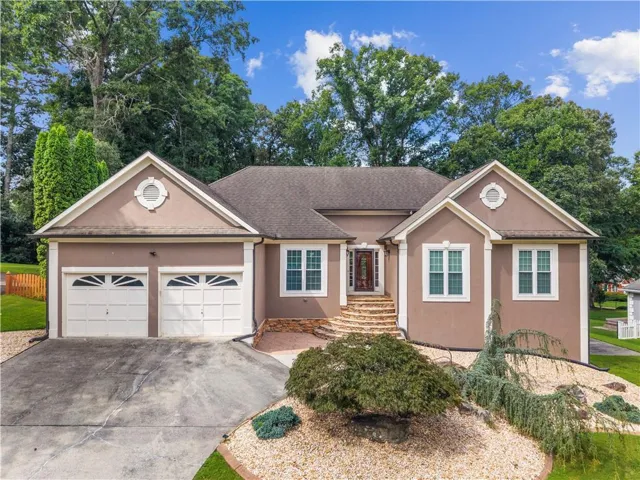 Stucco exterior with decorative trim accents, a two-car garage, multi-pane windows, stone stairs, and a well-landscaped front yard