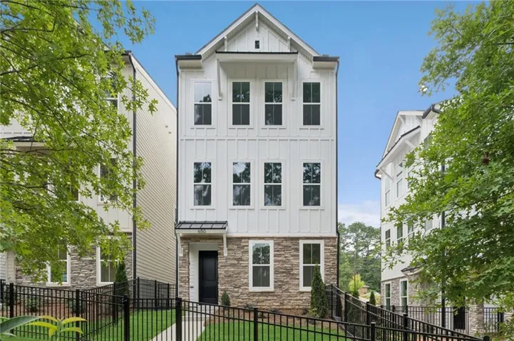 Three-story white board-and-batten exterior with stone accents, black metal fencing, and a dark entry door