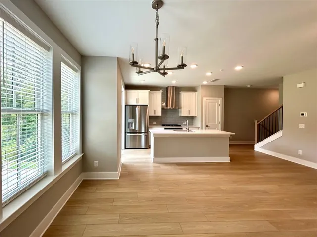 Kitchen with a chandelier, stainless steel fridge with ice dispenser, an island with sink, light wood-style floors, and wall chimney exhaust hood