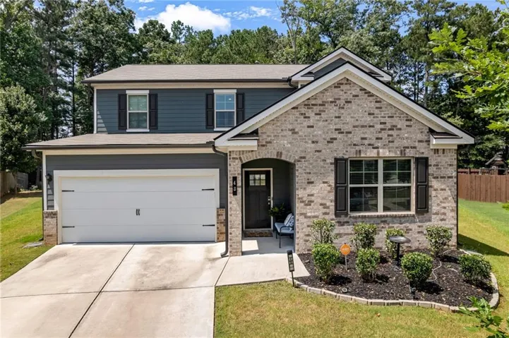 Two-story residence featuring a brick and siding exterior, an arched entry, a two-car garage, and landscaped front planting beds