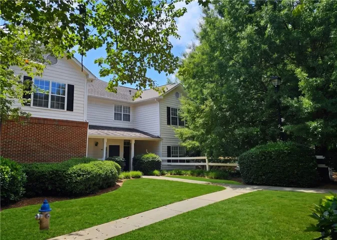 White siding exterior with brick accents, covered front entry, established landscaping, and a manicured lawn