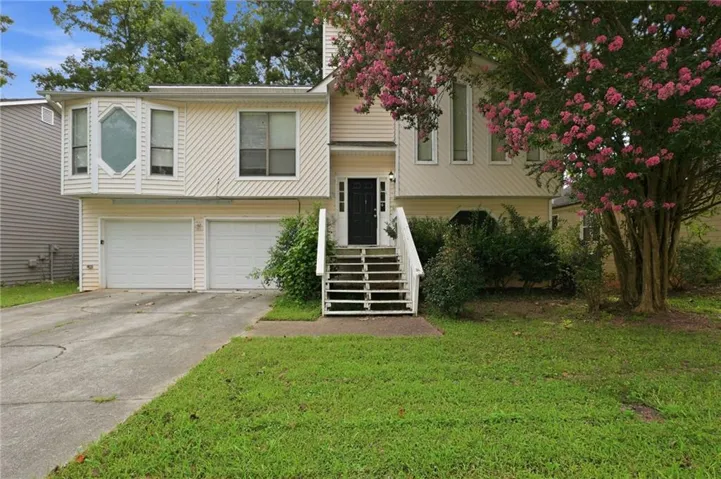 Two-car garage, light-colored horizontal siding, prominent bay window, white-painted entry stairs with handrails, and mature landscaping