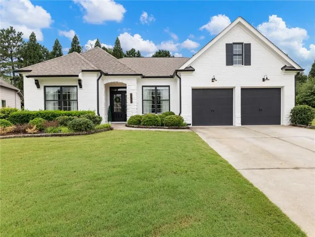 White brick exterior with dark trim accents, featuring a two-car garage with dark paneled doors, black-framed windows, and a covered entry