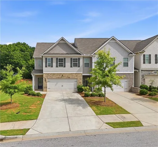 Contemporary townhome exterior featuring a two-car garage, brick and siding facade, dark shutters, and a mature tree