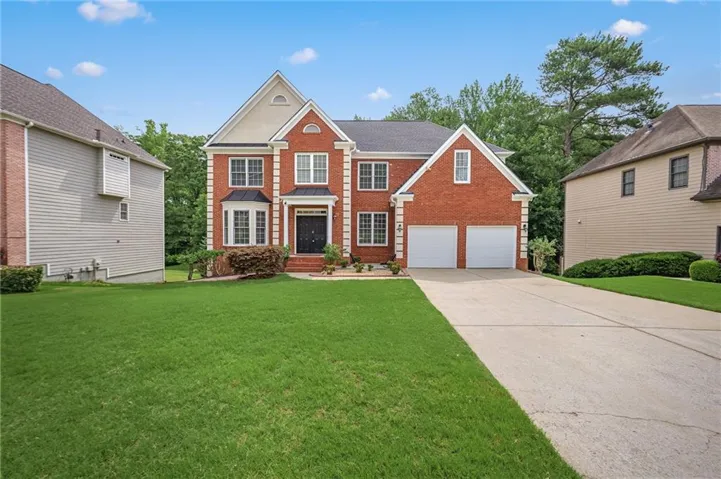 Brick exterior with white trim accents, a two-car garage, a bay window, and a spacious front lawn