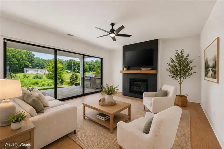 Spacious living area featuring large sliding glass doors, a modern fireplace with a dark surround, a wooden mantel, and light wood-finish flooring