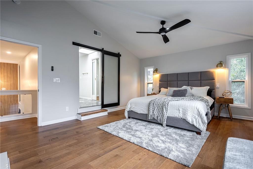 Bedroom with a barn door, dark hardwood / wood-style floors, ceiling fan, and lofted ceiling